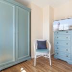 Schlafzimmer mit Kleiderschrank, Stuhl und TV auf Kommode.