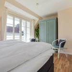 Schlafzimmer mit Doppelbett, Fenster, Kleiderschrank und Fernseher.
