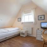 Schlafzimmer mit Dachschräge, Bett, TV und Schreibtisch.
