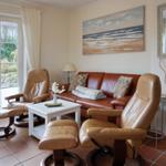 Wohnzimmer mit Ledersofa und zwei Sessel, großes Fenster, Wandbild und Spiegel.