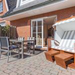Terrasse mit Gartenmöbeln und Strandkorb vor einem Haus mit Backsteinfassade.