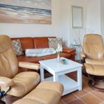 Lounge mit zwei Ledersessel, Sofa und Tisch. Wandbild zeigt Strand.
