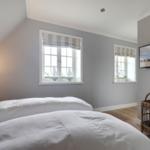 Schlafzimmer mit Bett, zwei Fenstern und Fernseher an der Wand.