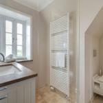 Badezimmer mit Waschbecken, Fenster und Heizkörper. Toilette im Anschluss.