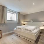Schlafzimmer mit weißem Bett, Holzboden und Fenster mit Vorhängen.