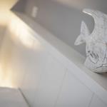 Ein weißes Fischdekoration steht auf einem weißen Kopfteil neben einer Lampe.