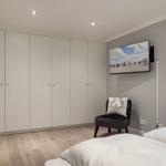 Schlafzimmer mit weißem Kleiderschrank, Bett und Wandfernseher.