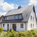 Modern villa with white walls and dark roof. Garden with plants and flowering blooms.