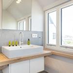 Bathroom with sink, mirror, and window. Wooden surface and gray wall.