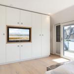 Bedroom with TV in wall and balcony view of thatched roof house
