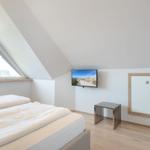 Bedroom with sloped ceiling, bed, TV, and wardrobe.