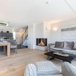Living room with fireplace, sofa, and dining table. Kitchen in background.