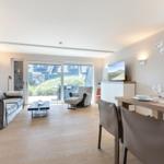 Living and dining area with wooden floor, sofa, TV, and table with chairs.