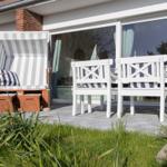 Terrace with beach chair and white chairs. Glass facade and greenery in the background.