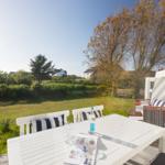White table with chairs and lounge chair on terrace with view of lawn and trees.