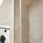 Shower with glass enclosure and washing machine in bathroom