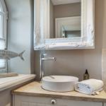 Badezimmer mit Waschtisch, Spiegel und Fenster. Dekoration: Fischfigur und Handtuch.