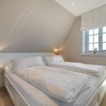 Schlafzimmer mit Doppelbett, Fenster und Nachttisch.