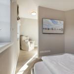 Schlafzimmer mit Bett, Fernseher und Sitzgelegenheit. Fensterbank mit Vogeldekoration.