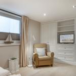Ein Schlafzimmer mit Bett, Sessel, TV und Fenster mit Segelboot.
