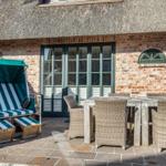 Terrasse mit Strandkorb und Esstisch vor einem Haus mit Strohdach und Backsteinmauer.