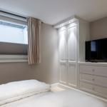 Schlafzimmer mit weißem Bett, Kleiderschrank und Fernseher.