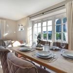 Esszimmer mit Tisch, Stühlen und Fenstern. Anrichten und Dekoration sind sichtbar.