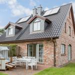 Haus mit Terrasse, weißem Tisch und Stühlen, Strandkorb und grünem Rasen.