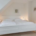 Schlafzimmer mit weißem Bett, zwei Nachttischen und Bildern an der Wand.