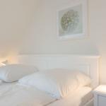 Schlafzimmer mit weißem Bett, Nachttisch und Wandbild.