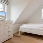 Schlafzimmer mit weißem Bett, Schrank und Fernseher. Holzboden und schräge Wand.
