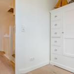 Weißer Schrank mit Schubladen und Tür. Blick in Schlafzimmer mit Bett und Fenster.
