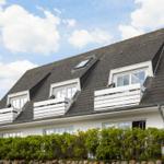 House with dormer windows and white balconies under blue sky.