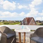 Terrace with table and two chairs. View of houses and green areas under blue sky.