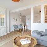 Living and dining area with wooden floor, sofa, and kitchen cabinets.