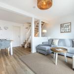 Living and dining area with sofa, table and chairs. Staircase and wall decoration visible.