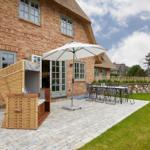 Terrasse mit Loungemöbeln, Sonnenschirm und Gartenhaus an einem traditionellen Haus.