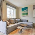 Wohnzimmer mit grauem Sofa, Holzboden und Fenstern.