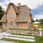 Haus mit Strohdach, Steinmauer und Gartenbereich mit Liege.
