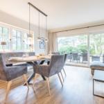 Essbereich mit Tisch und Stühlen. Wohnbereich mit Sofa und Couchtisch. Glasfront zum Garten.