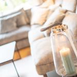 Ein Glasleuchter mit brennender Kerze steht vor einem Sofa mit Kissen.