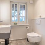 Badezimmer mit Waschbecken, Toilette und Dusche. Fenster mit Blick nach außen.