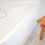 Eine weiße Badewanne mit Duschkopf und hölzerner Bank.