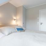 Schlafzimmer mit Bett, Kopfteil und Wandlampen. Tür und Schrank sind sichtbar.