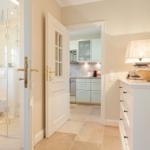 Hallway with bedroom, kitchen, and bathroom. White furniture and stone tiles.