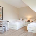 Two beds, desk, and wall art in an attic room.