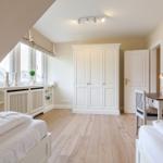 Room with two beds, desk, and wardrobe. Wooden floor and large window.