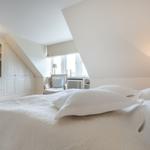 Bedroom with sloped ceiling, bed, TV, and armchair.
