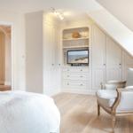 Bedroom with sloped ceiling, white closet, and armchair.