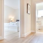Bedroom and bathroom accessible via hallway. Wooden floor and white walls.